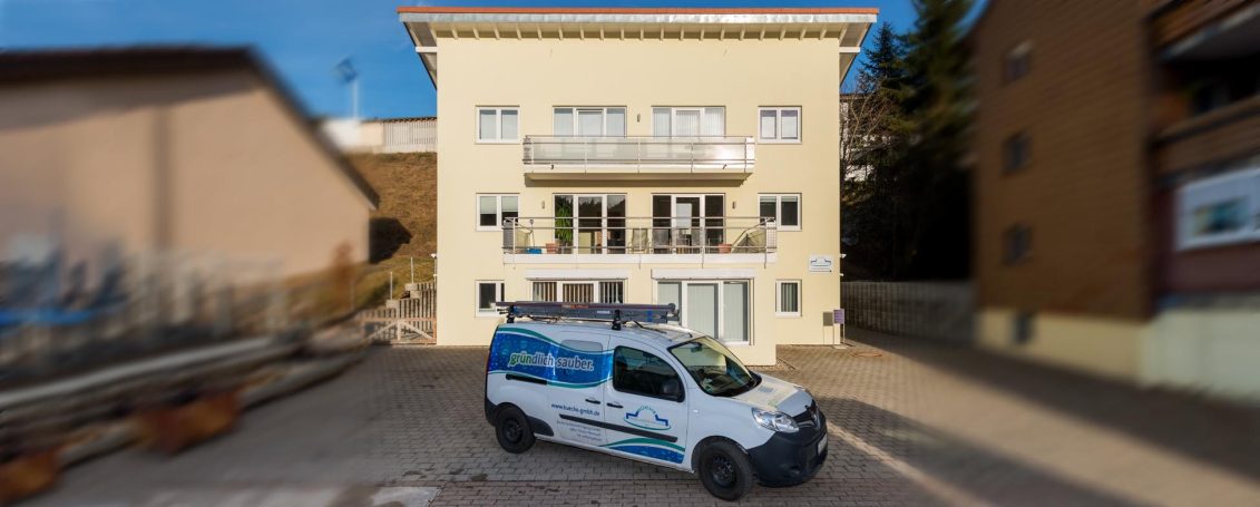Ein Lieferwagen vor einem mehrstöckigen, hellen Gebäude in einer städtischen Umgebung.